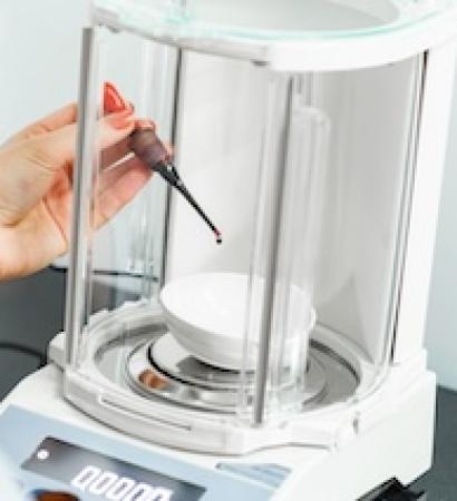Precision weighing of liquid in a laboratory setup with an analytical balance during a research experiment A researcher carefully measures an accurate amount of liquid using an analytical balance in a laboratory environment. The setup is precise and methodical, ensuring accurate results.